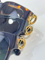 Sunglasses close-up: gold LV hinge details on dark frame with tinted lens