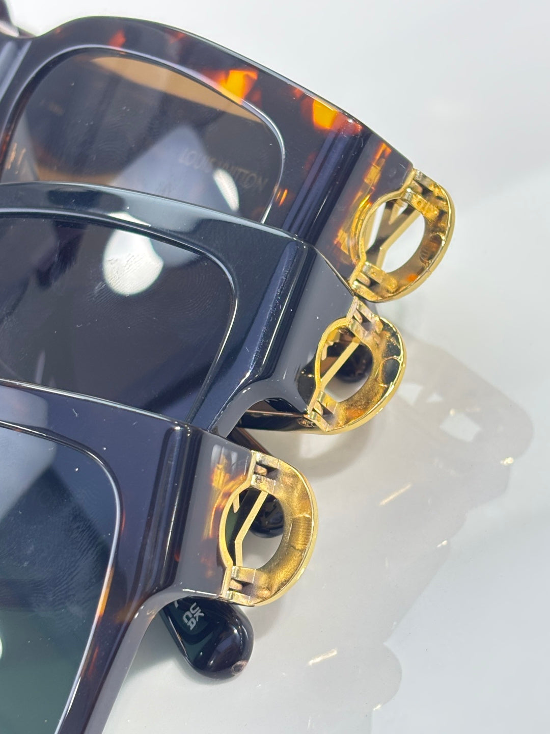 Sunglasses close-up: gold LV hinge details on dark frame with tinted lens