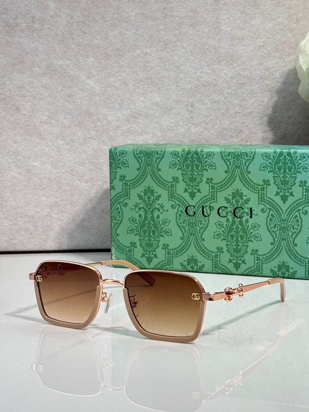 Gucci sunglasses with dark brown frames, gold accents, and warm beige gradient lenses