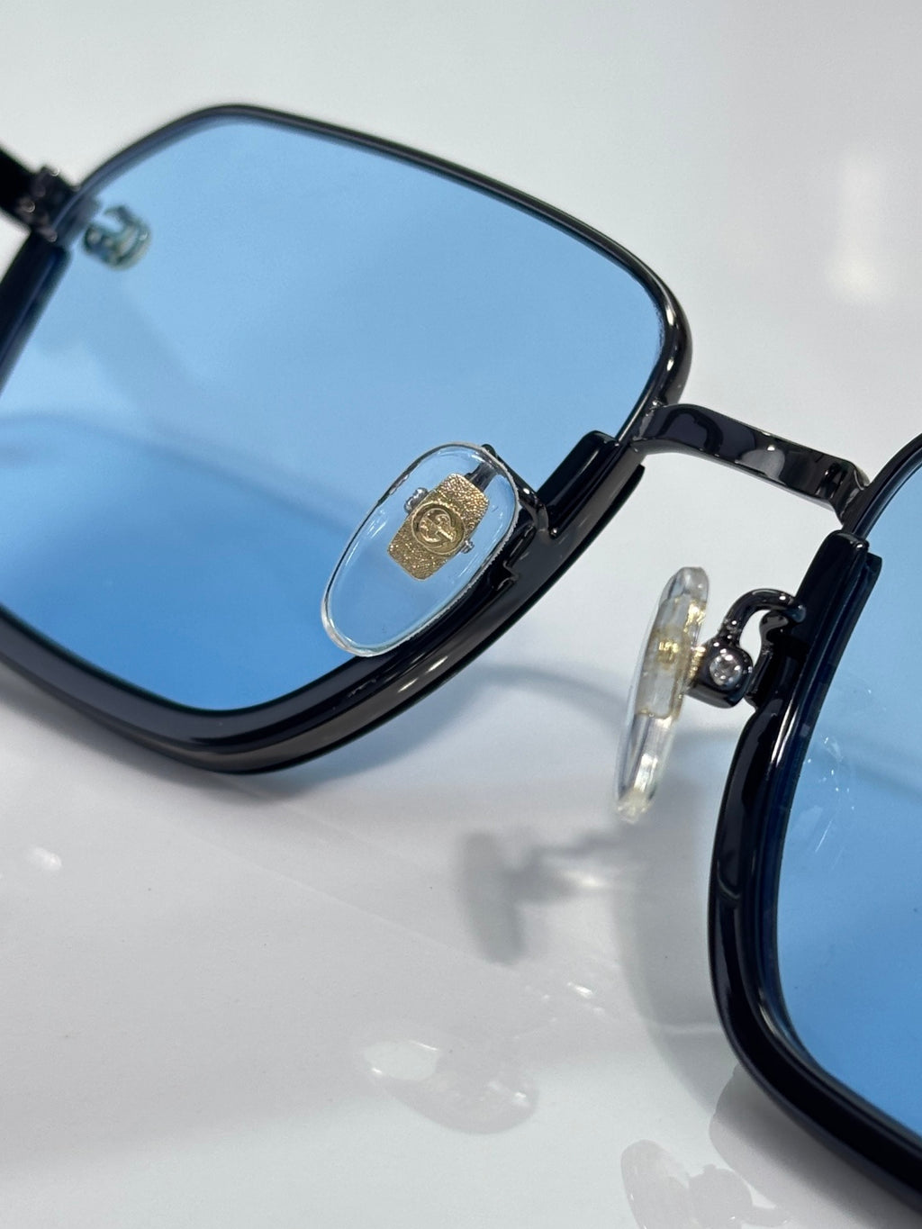 Gucci sunglasses close-up: black frames with blue gradient lenses and gold logo tab