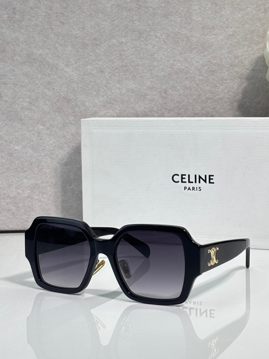 Black rectangular sunglasses at an angle with dark lenses and gold logo on the temple