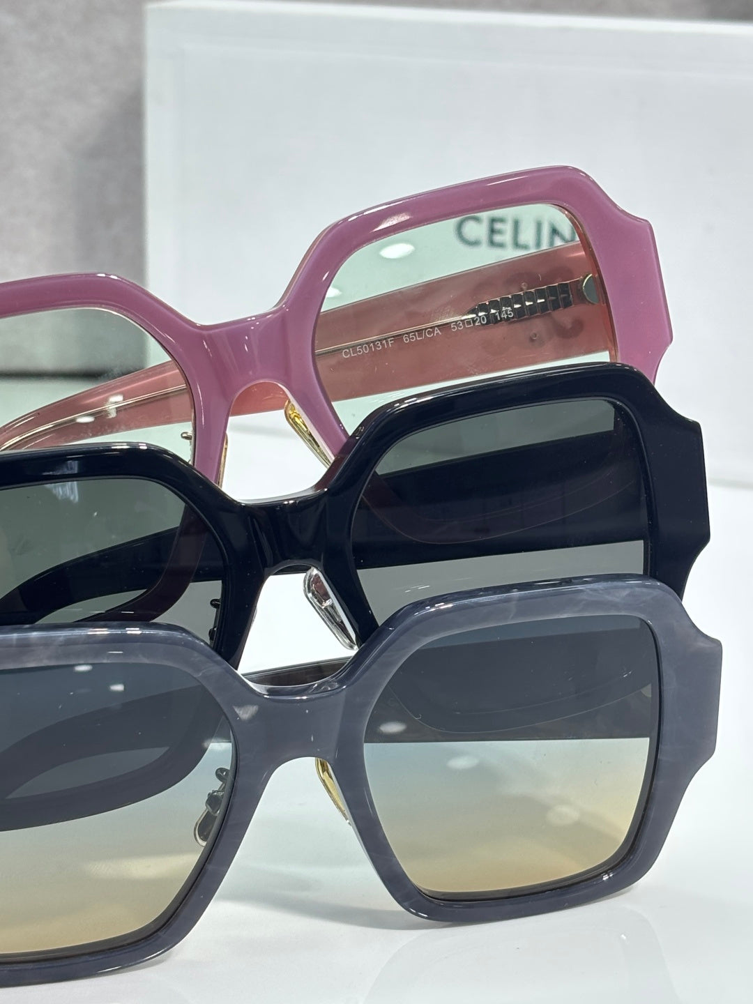 Stack of rectangular sunglasses in maroon, black, and navy with gold logo temples