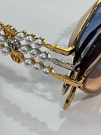 Gucci sunglasses close-up: gold temple with pearl bead chain and blue-tinted lens