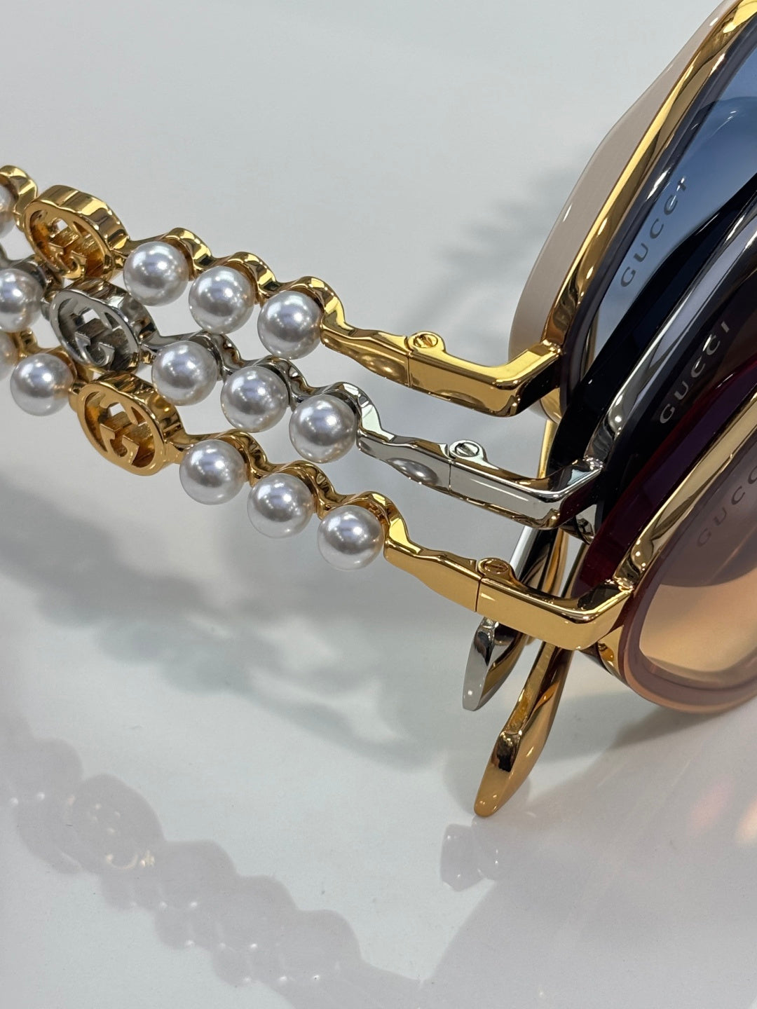 Gucci sunglasses close-up: gold temple with pearl bead chain and blue-tinted lens