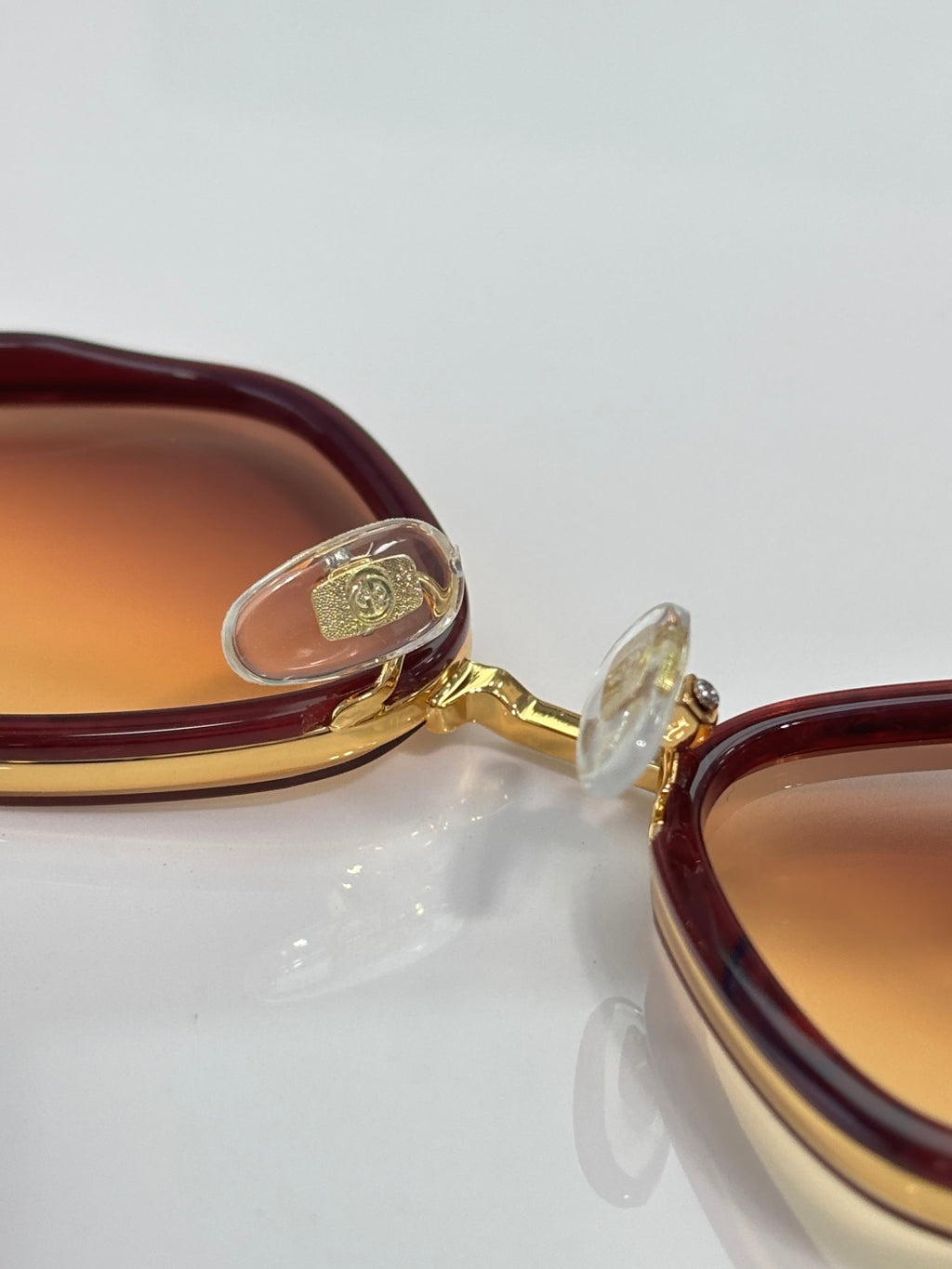 Gucci sunglasses close-up: gold hinge and emblem on maroon-burgundy frame
