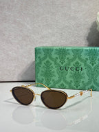 Gold oval sunglasses with deep brown lenses and decorative chain-link arms