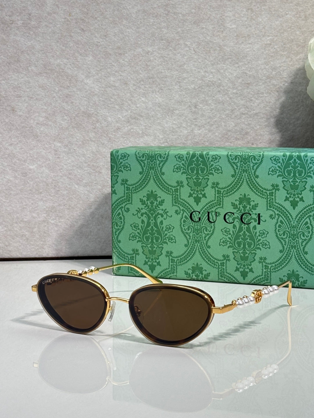 Gold oval sunglasses with deep brown lenses and decorative chain-link arms