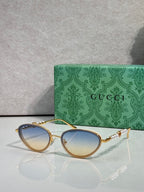 Gold oval sunglasses with pale blue gradient lenses and jeweled chain-link arms