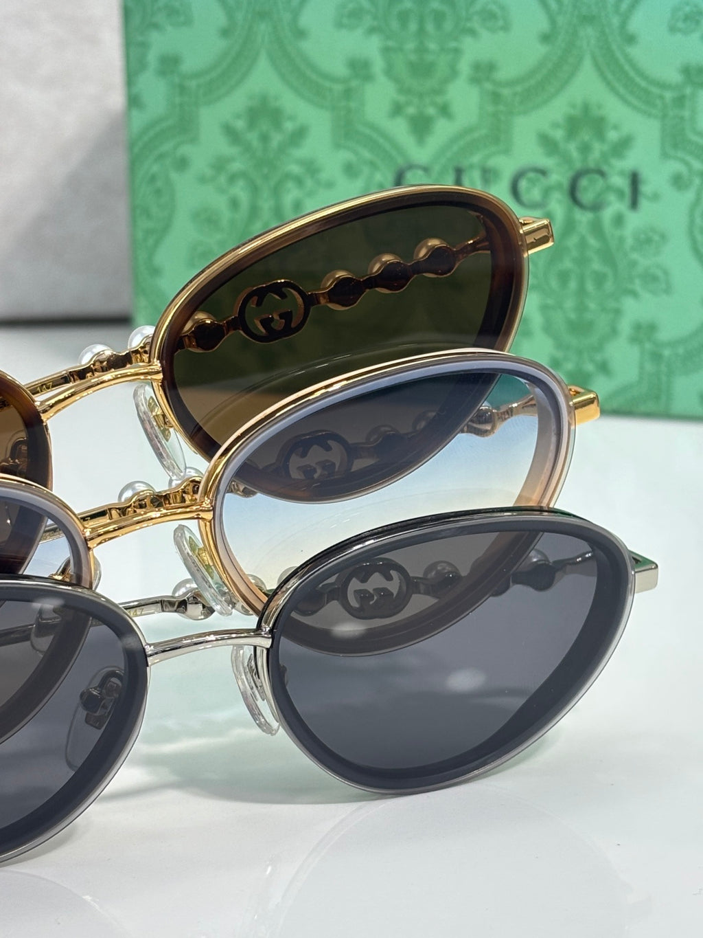 Oval sunglasses with gold frames and dark lenses, stacked with studded arms