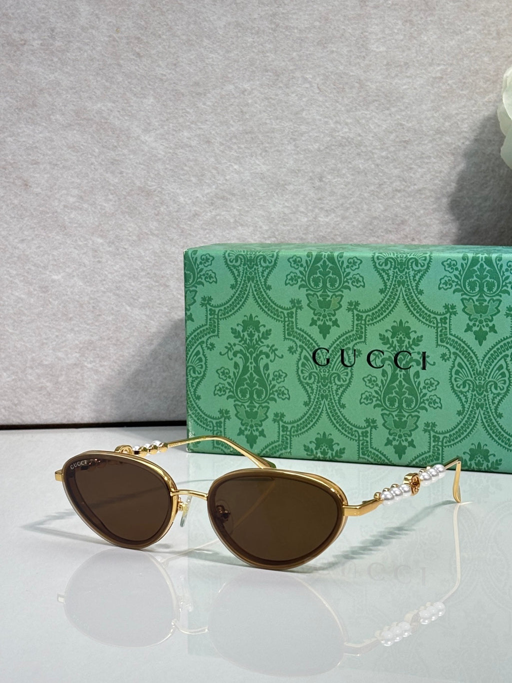 Gold oval sunglasses with dark brown lenses and decorative chain-link arms