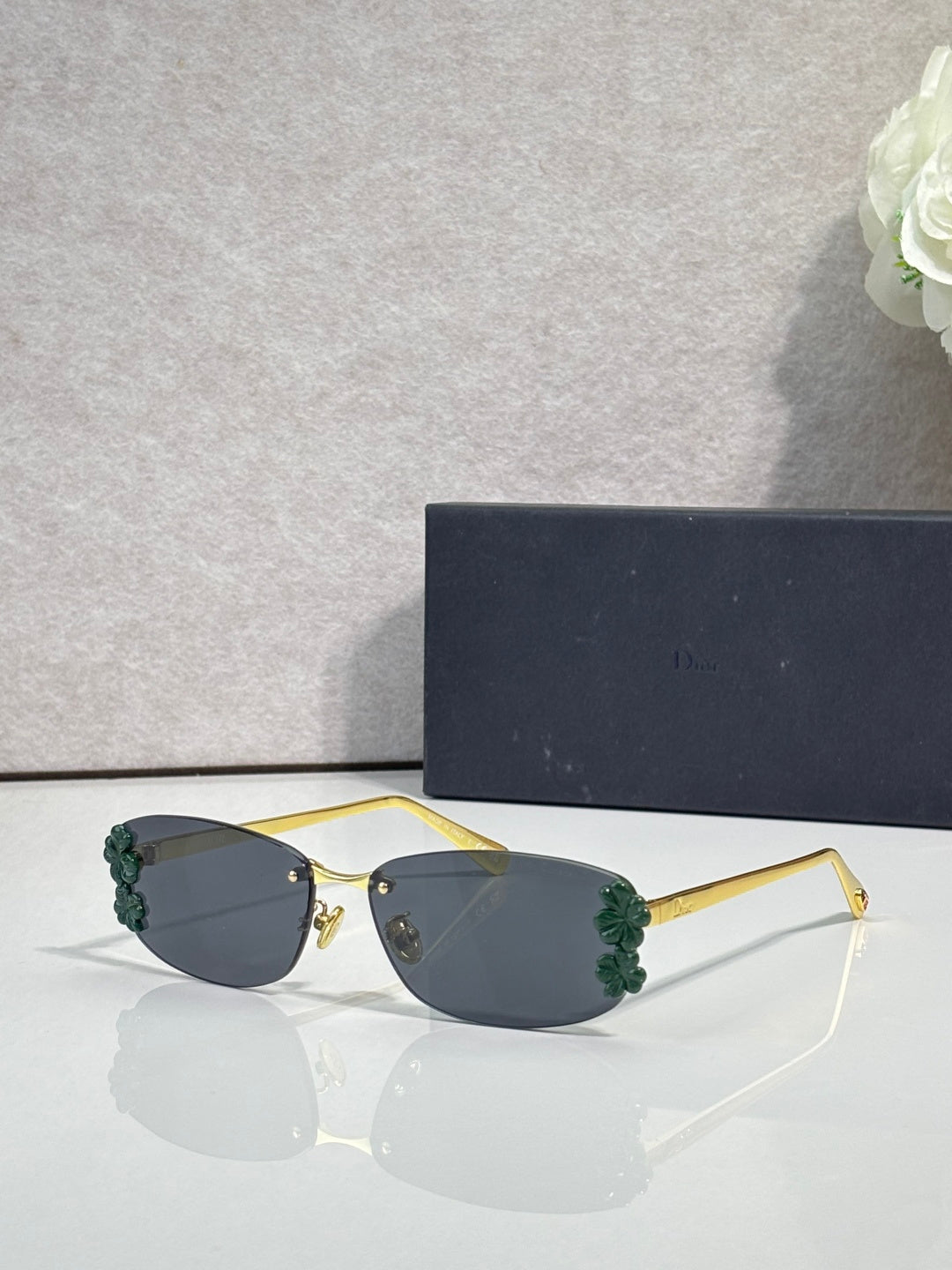 Dior sunglasses with dark lenses and gold frame, green floral details on temples