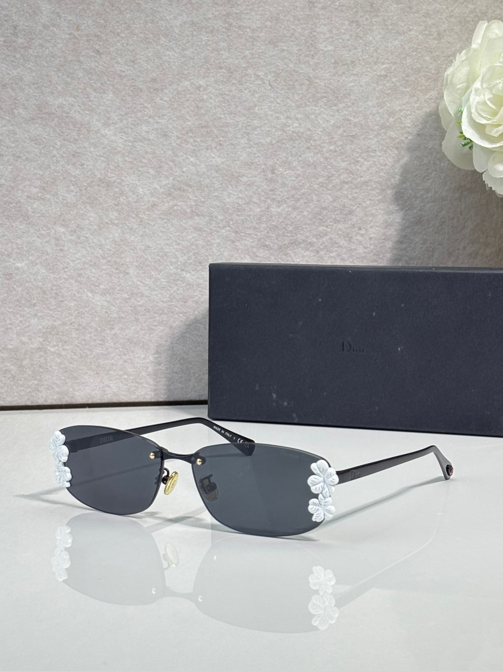 Dior sunglasses with dark lenses and black frame, white flower accents on temples