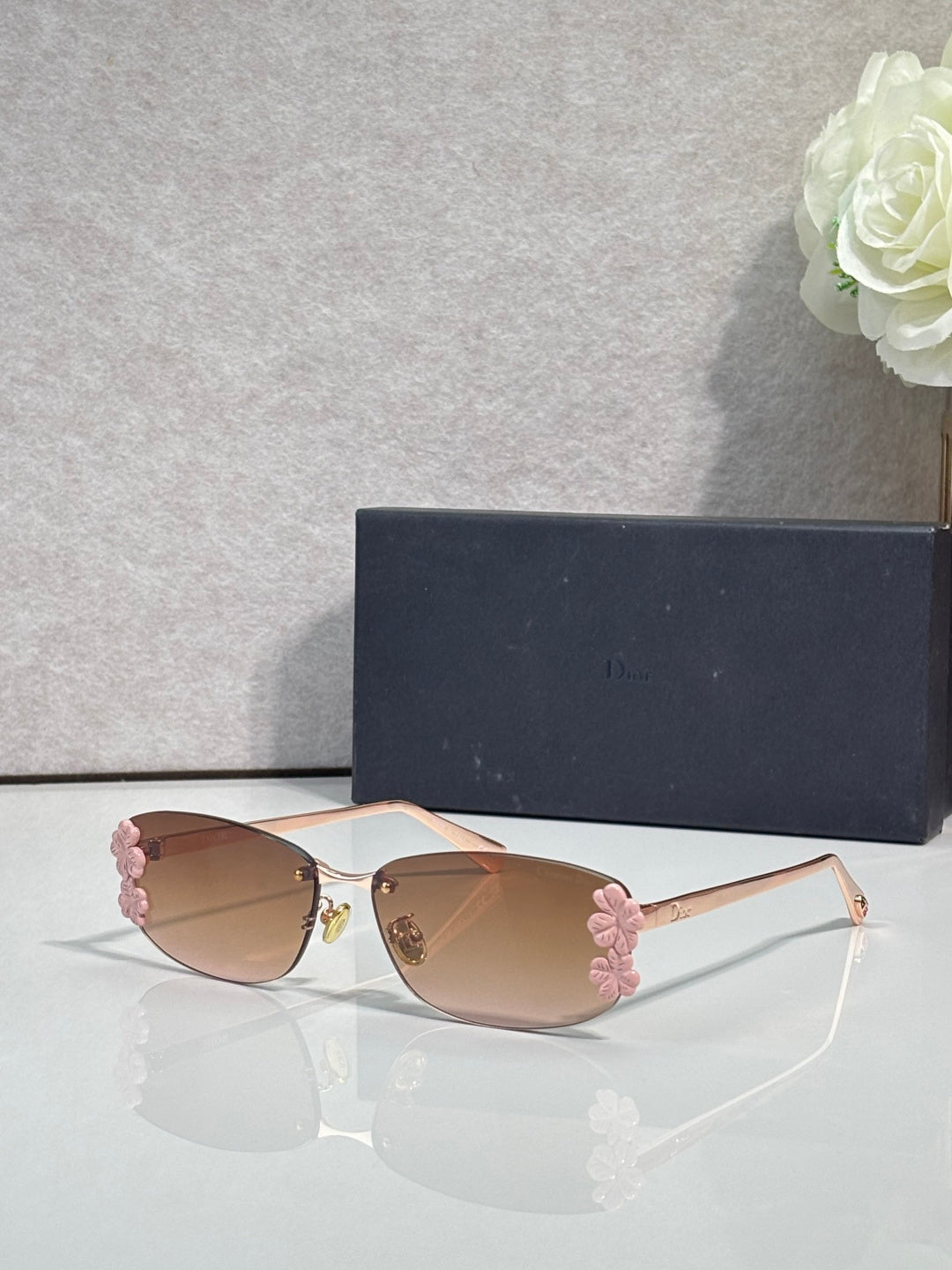 Dior sunglasses with tan lenses and pale frame, pink floral accents on temples