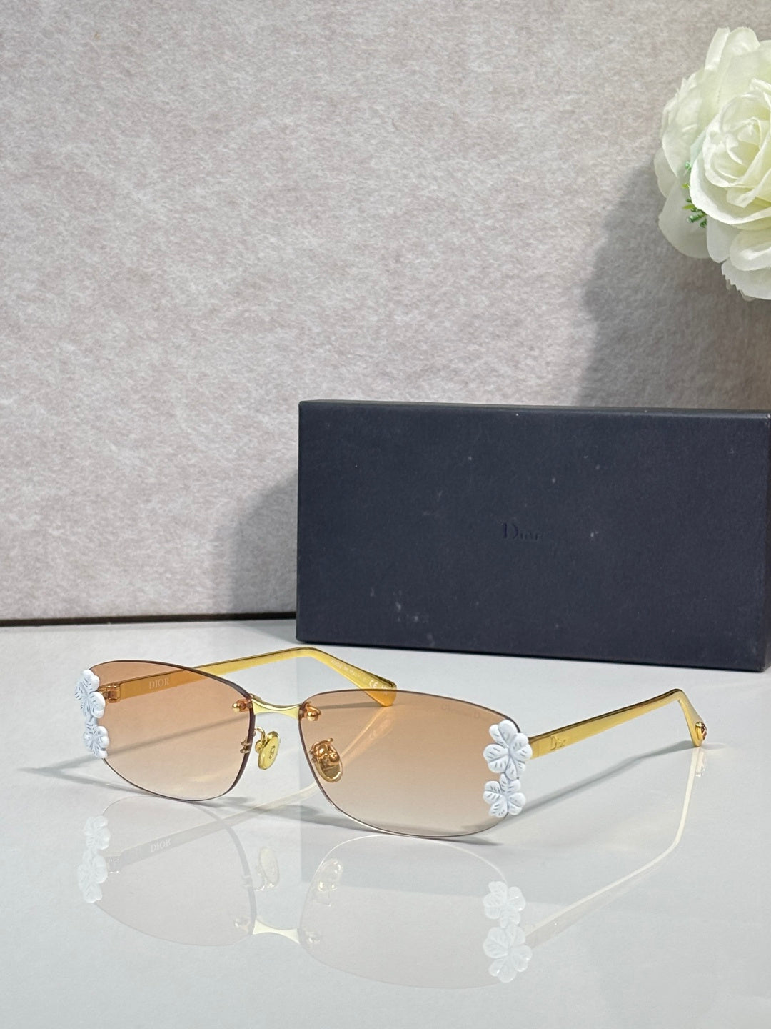 Dior sunglasses with amber lenses and gold frame, white flower accents on temples