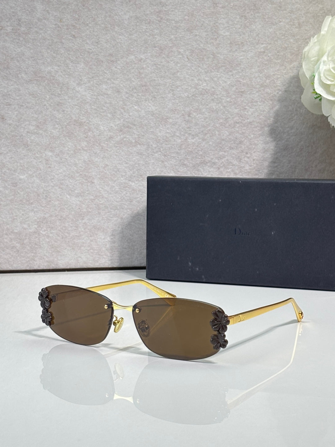 Dior sunglasses with brown lenses and gold frame, dark floral accents on temples