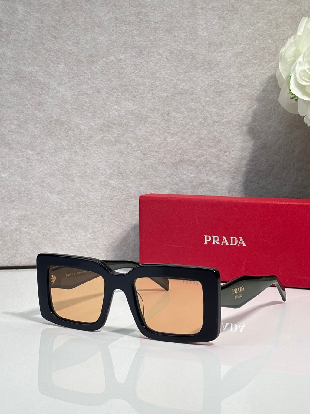 Prada sunglasses with thick black square frames and light tan-tinted lenses; Prada logo on temple