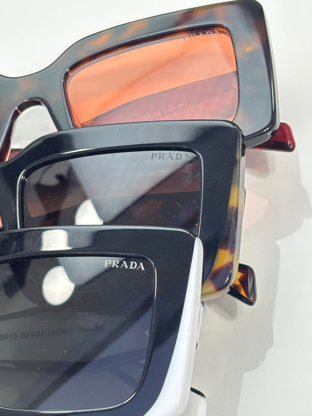 Prada sunglasses close-up: dark frames with orange-tinted lenses; Prada logo on lens