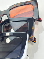 Prada sunglasses close-up: dark frames with orange-tinted lenses; Prada logo on lens