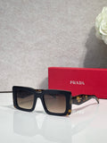 Prada sunglasses with thick black square frames and dark lenses; Prada logo on temple