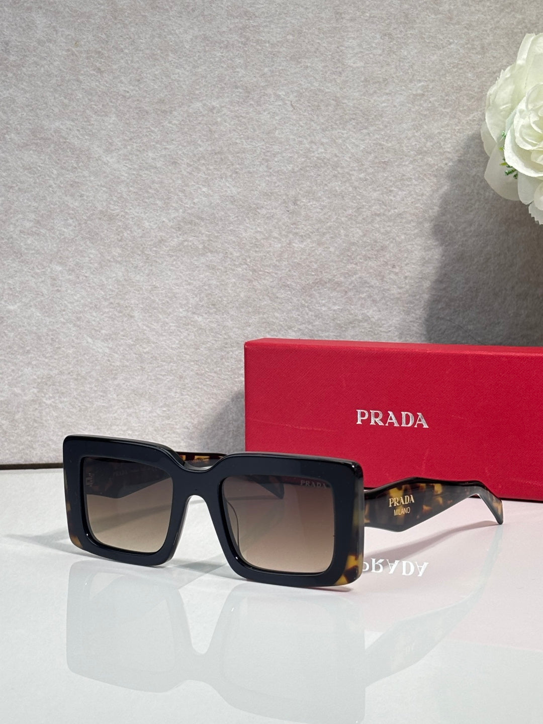 Prada sunglasses with thick black square frames and dark lenses; Prada logo on temple