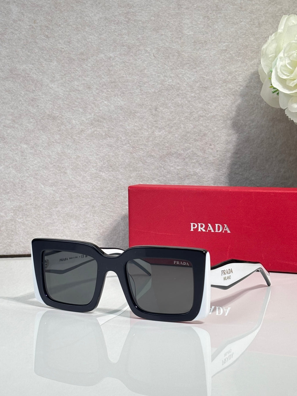 Prada sunglasses with thick black square frames and gray lenses; Prada logo on temple