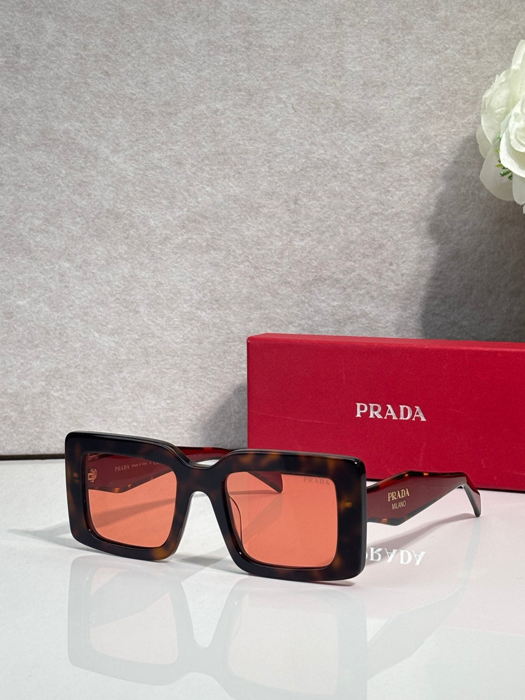 Prada sunglasses with thick black square frames and orange-tinted lenses; Prada logo on temple