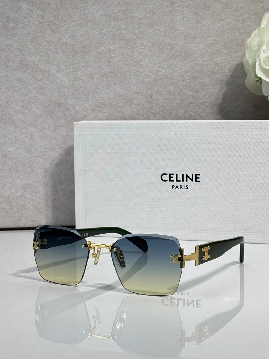 Square sunglasses with black frame and blue-green gradient lenses, gold logo hardware