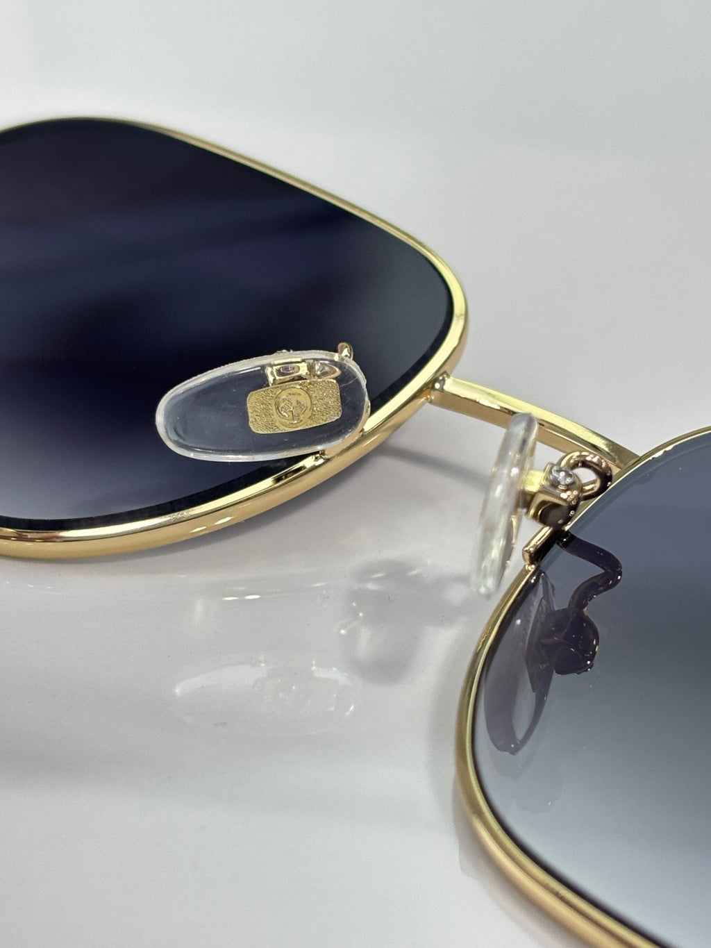 Gold-tone sunglasses hinge close-up with dark lens and small square logo