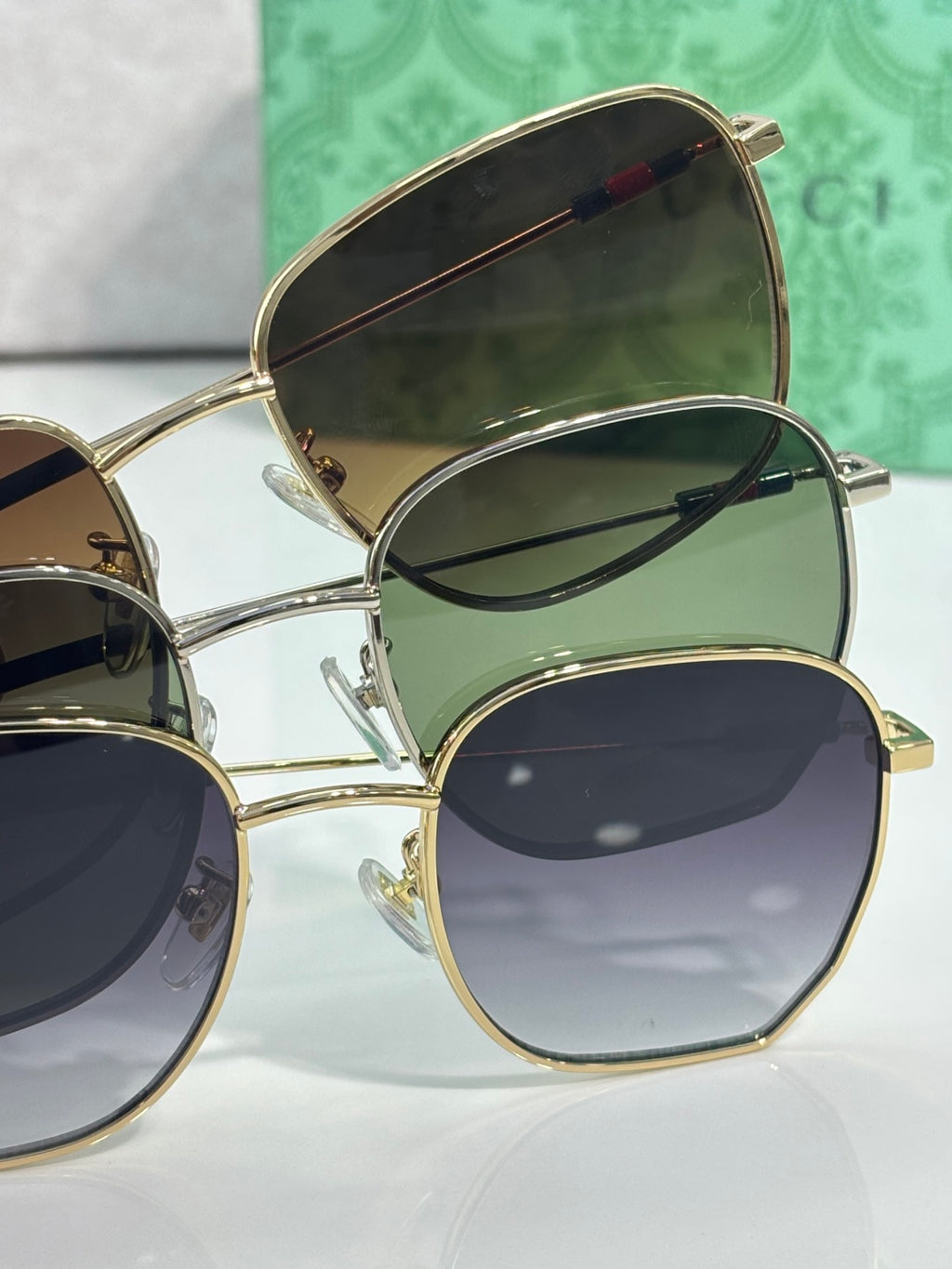 Stack of gold-tone square sunglasses with dark lenses and green-tinted frames