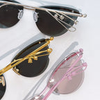 Sunglasses close-up with silver frame, black lenses, gold detail, and pink frame
