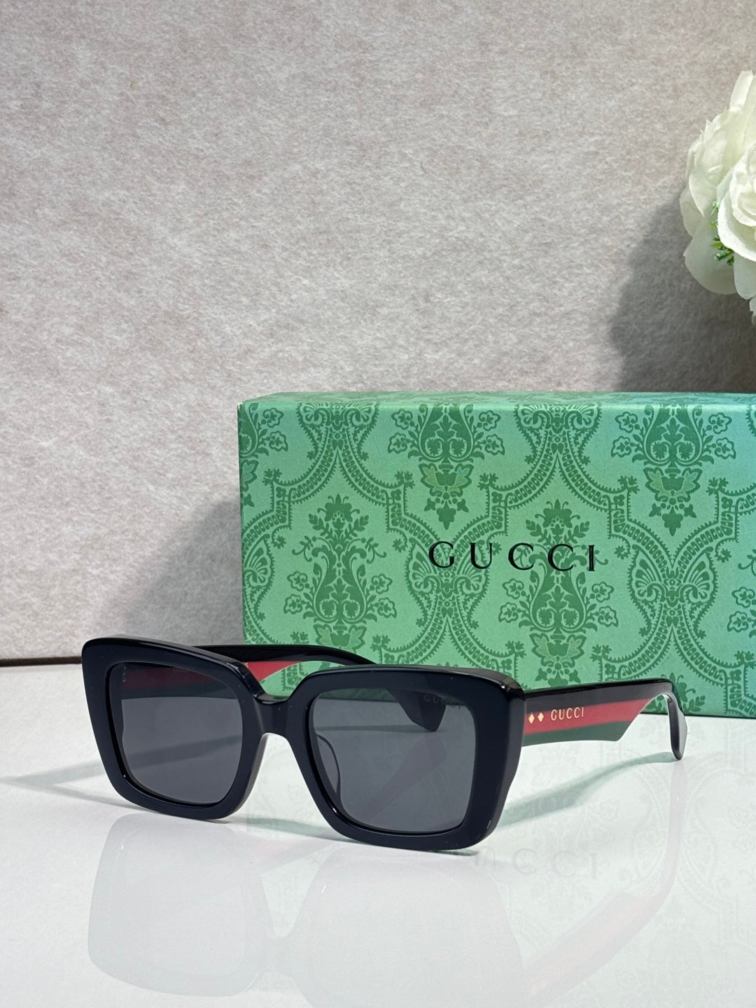 Gucci sunglasses with dark square frames and gray lenses, on a green logo case