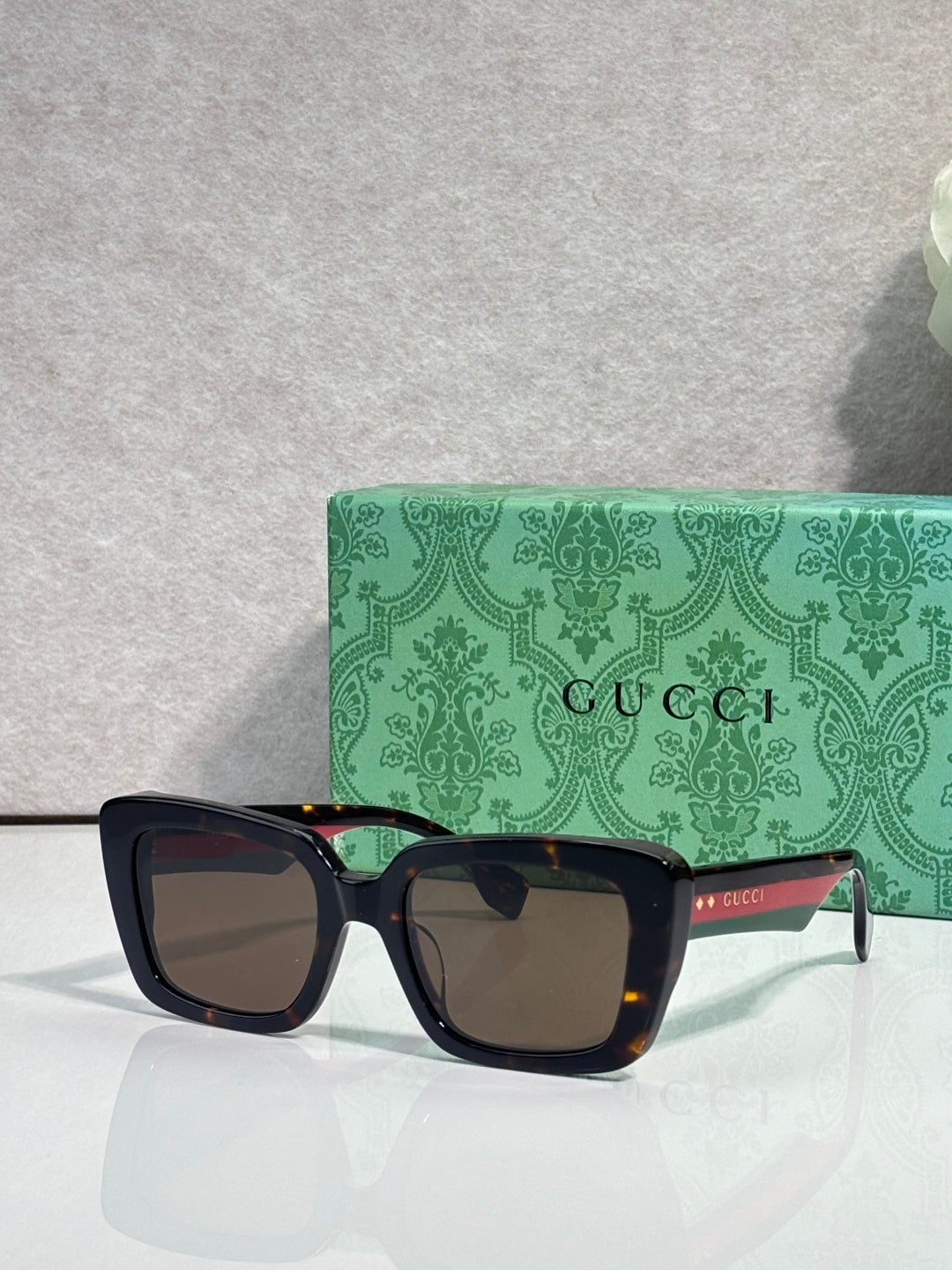 Gucci sunglasses with dark frames, brown-tinted lenses, and a green logo case behind