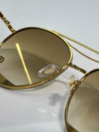 Close-up of gold-tone sunglass frame with engraved logo on temple