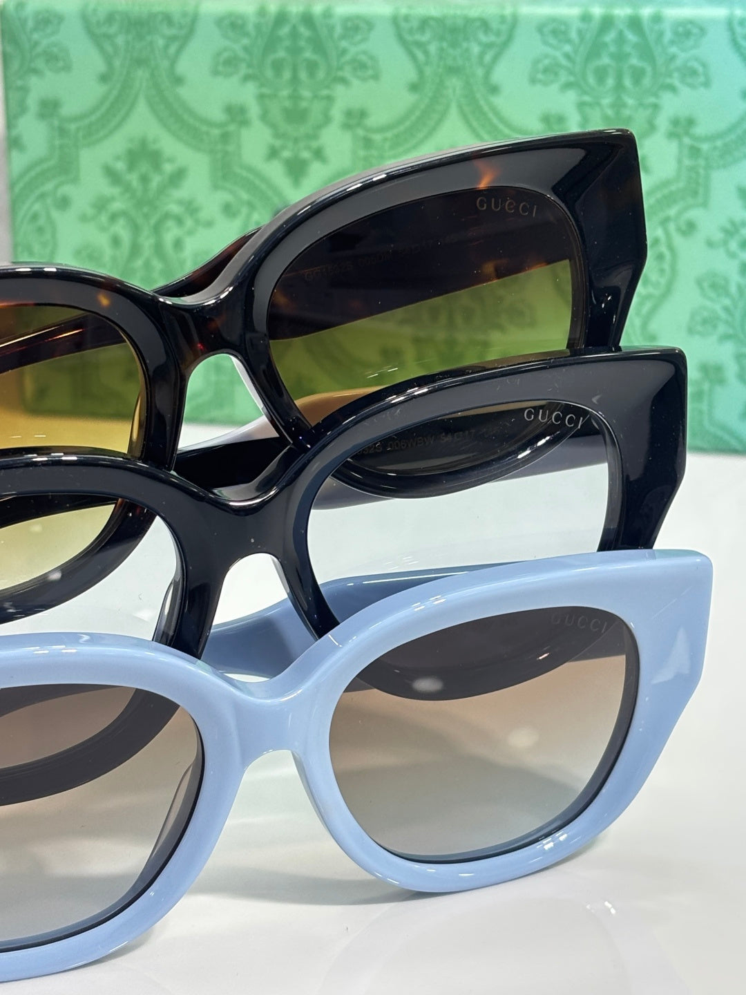 Gucci sunglasses pair in black and light blue frames, wide cat-eye silhouette, tinted lenses