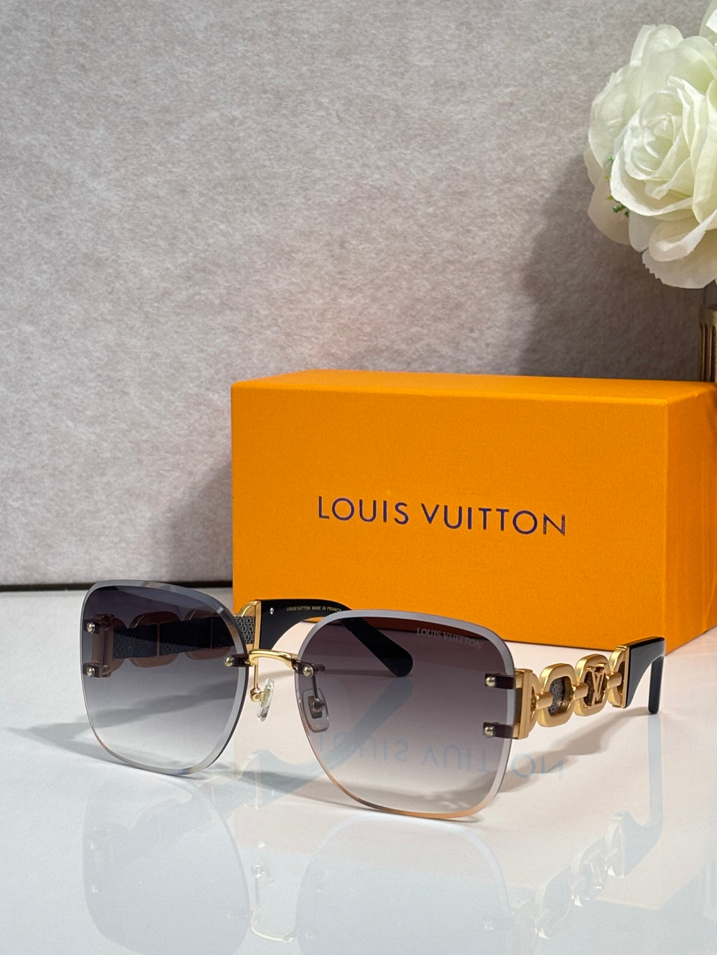 Sunglasses with rose-gold frame and dark tinted lenses; gold chain-link temple detail.