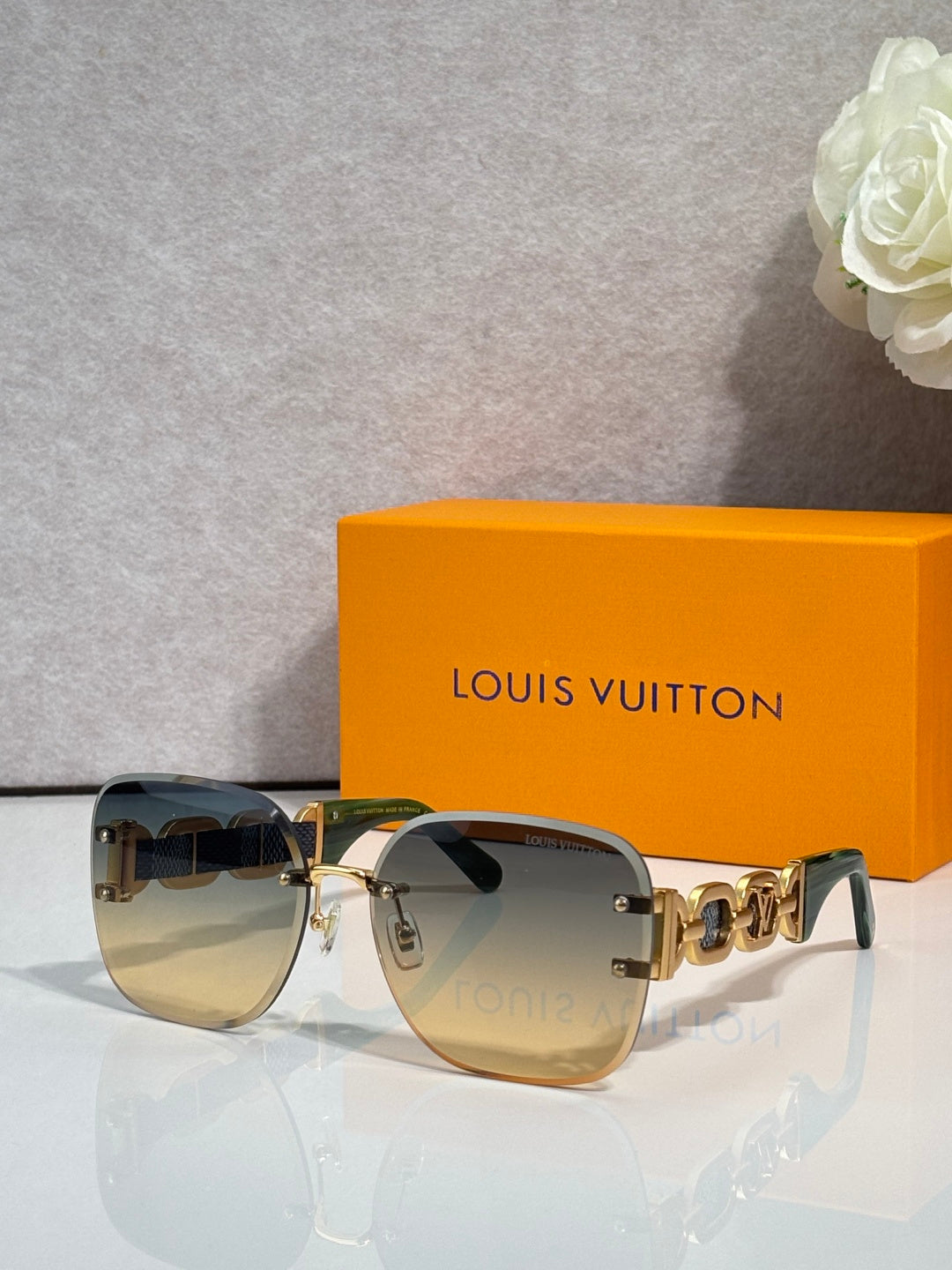 Sunglasses with dark olive-tinted lenses and gold frame; chunky chain-link temple detail.