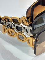 Sunglasses close-up: gold-tone chain-link temple with black insets and LV logo detail.