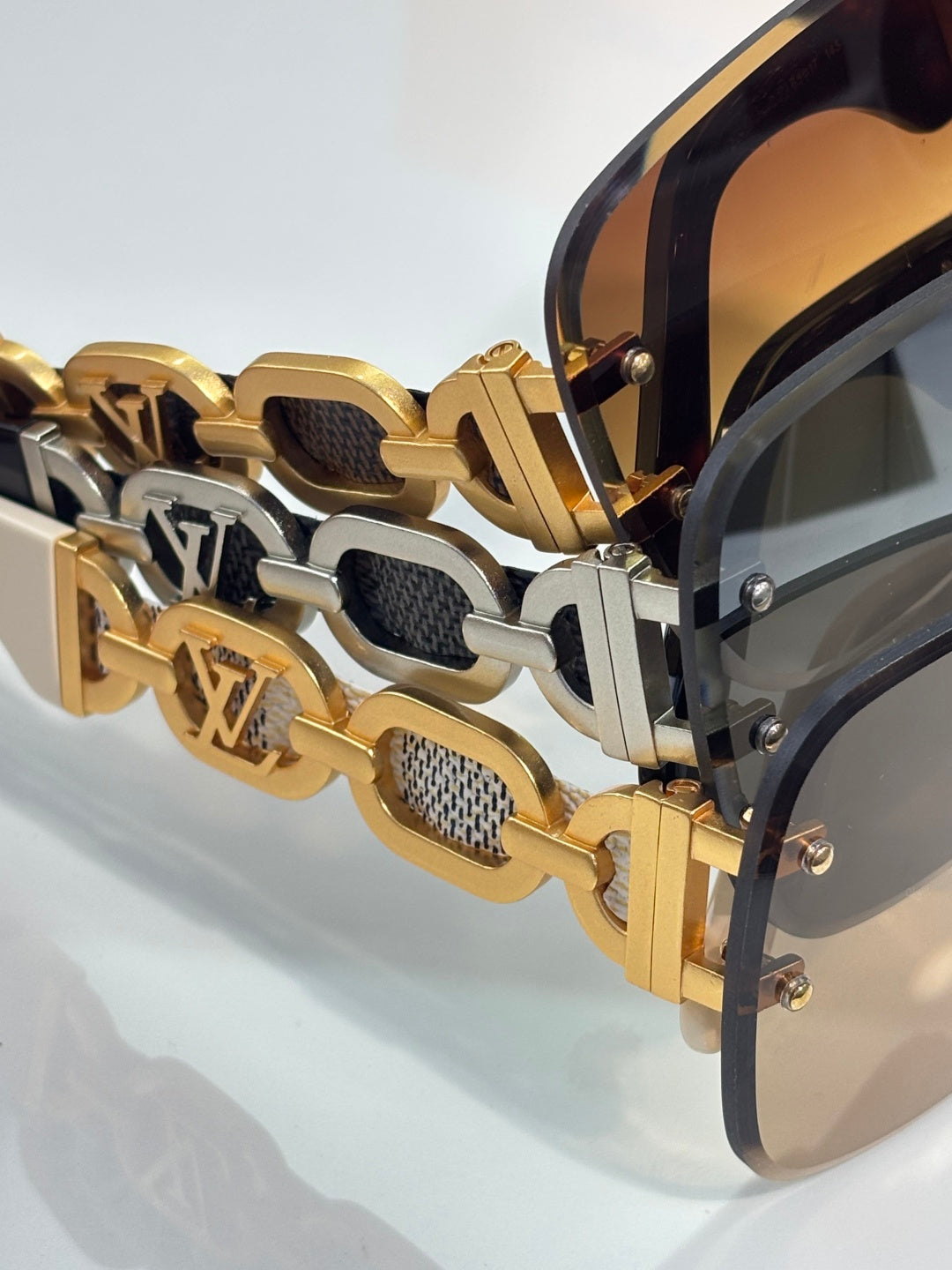 Sunglasses close-up: gold-tone chain-link temple with black insets and LV logo detail.