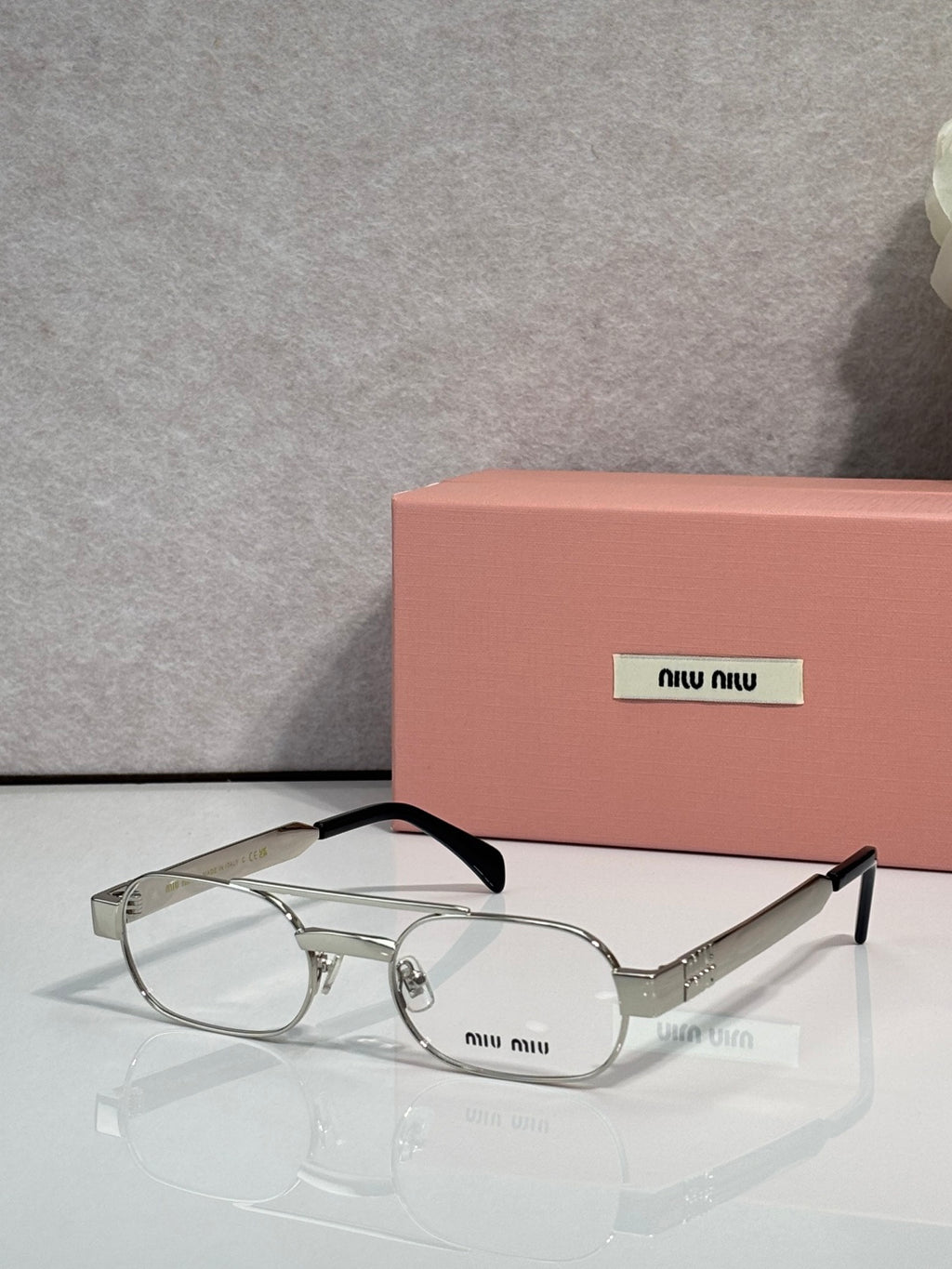 Silver eyeglasses with clear lenses and black temple arms, metal frame with small logo plate