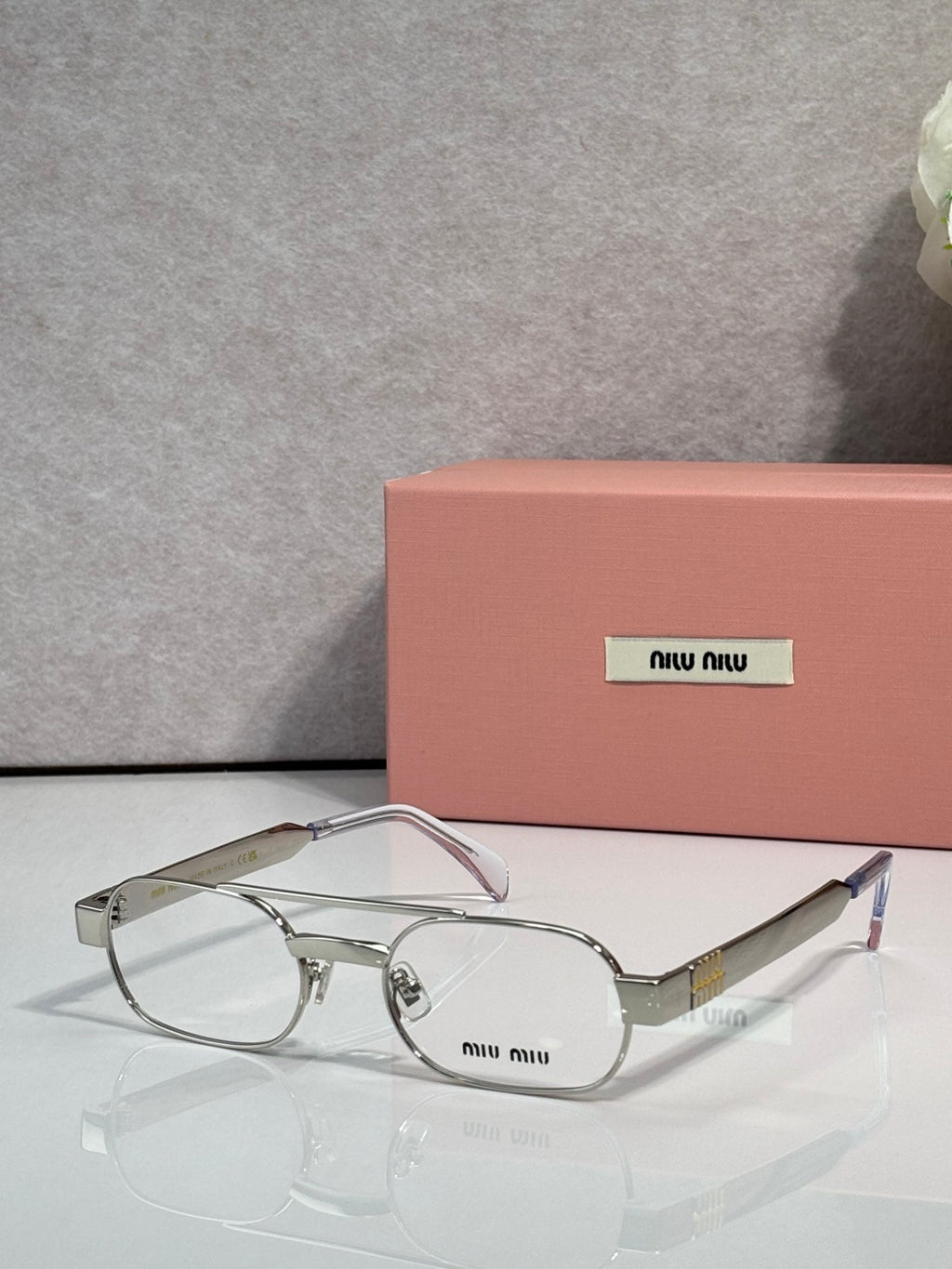 Silver eyeglasses with clear lenses and light pink temple arms, metal frame with logo plate