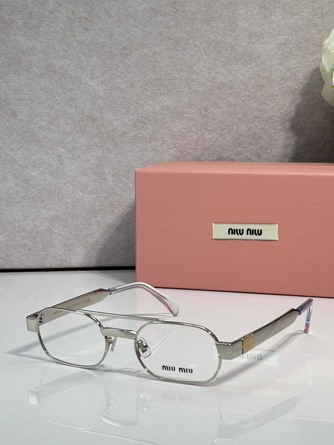 Silver eyeglasses with clear lenses and light pink temple arms, metal frame with logo plate