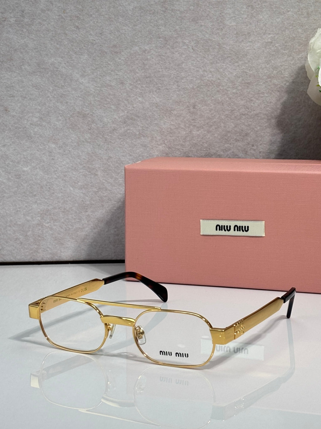Gold eyeglasses with clear lenses and light pink temple arms, slim metal frame and logo plate