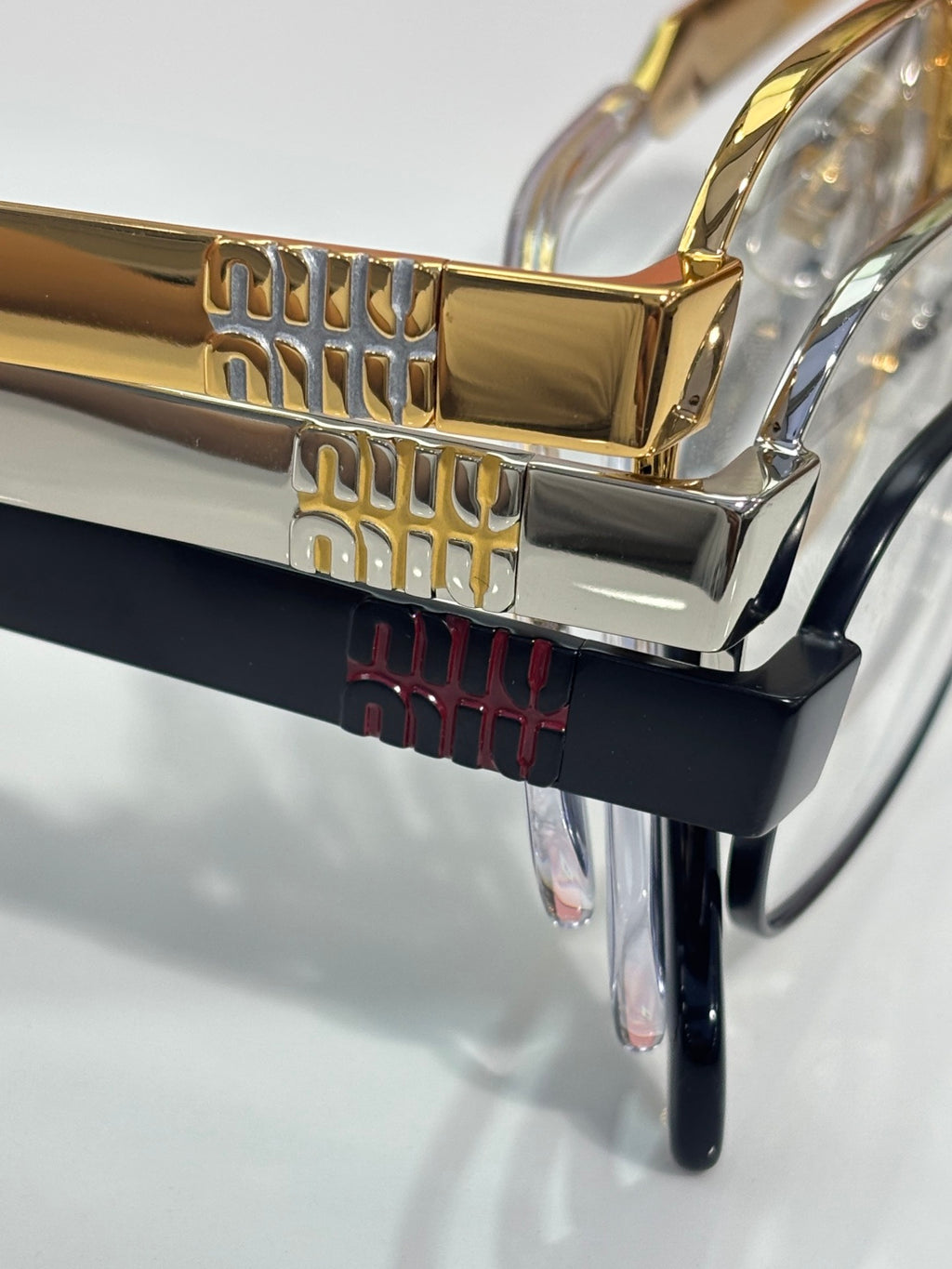 Gold eyeglasses frame with sculpted details and clear lens, with other colored frames behind