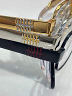 Gold eyeglasses frame with sculpted details and clear lens, with other colored frames behind
