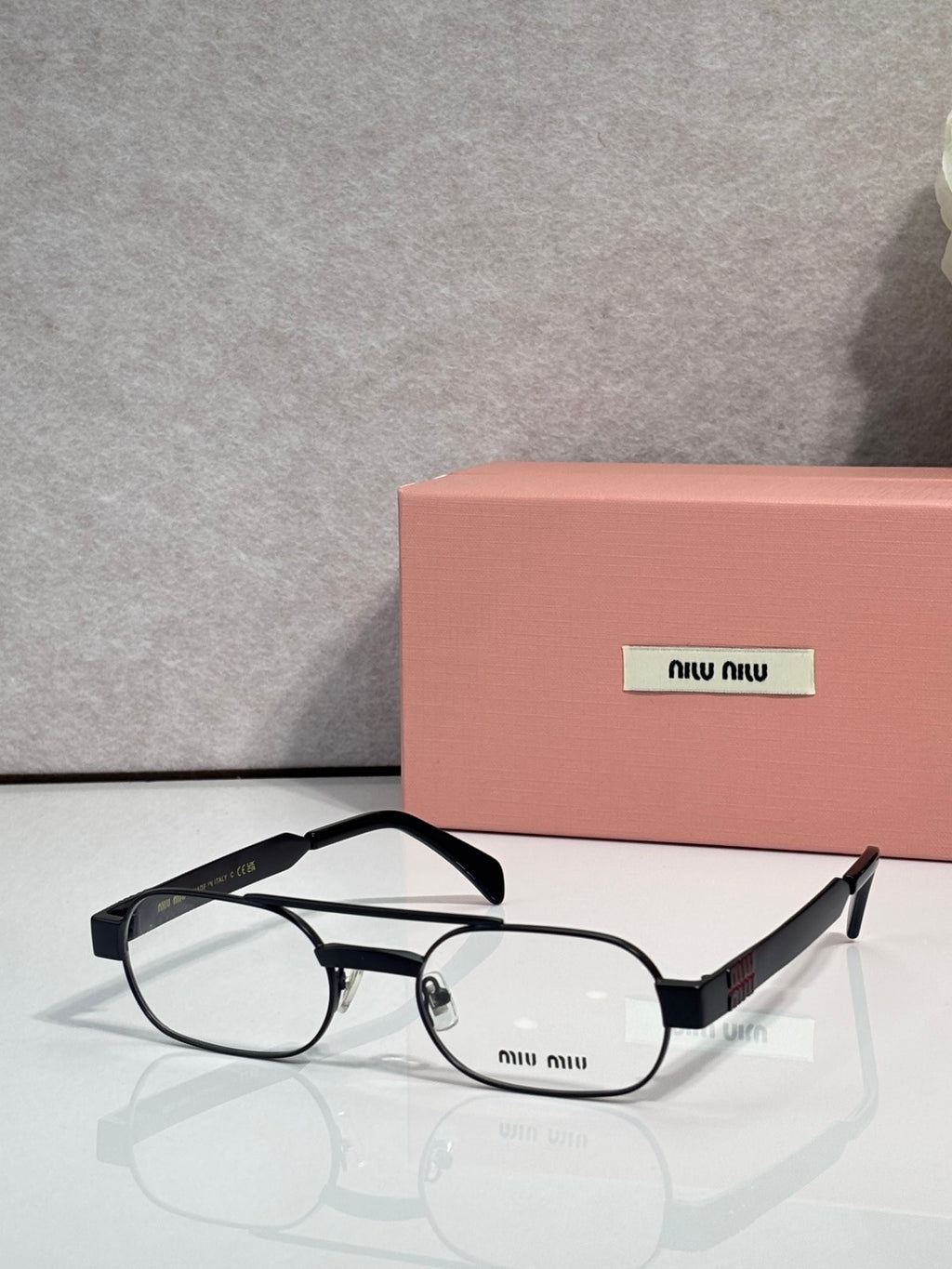 Black eyeglasses with clear lenses and black temple arms, metal frame with logo plate