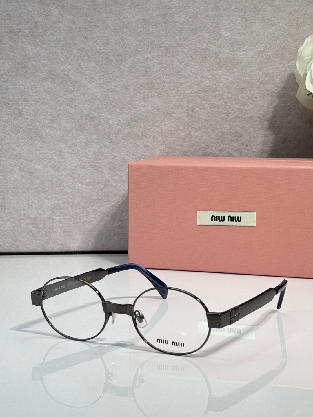 Round eyeglass frames with clear lenses, dark blue temples and silver metal, Miu Miu logo.