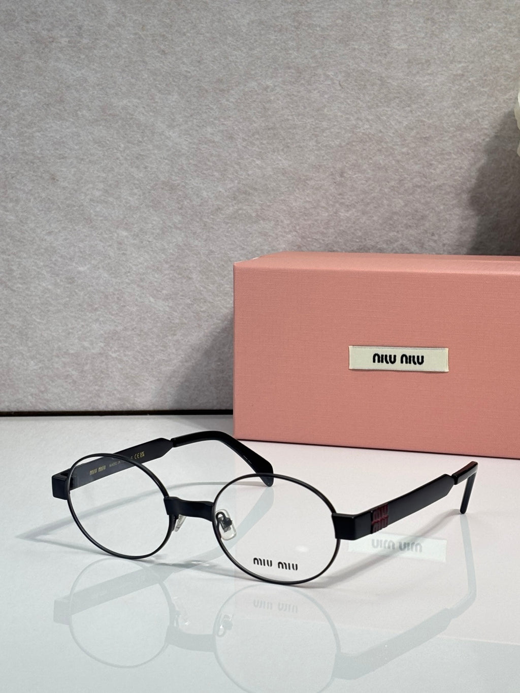 Round eyeglass frames with clear lenses, black arms and metal hinges, Miu Miu logo.