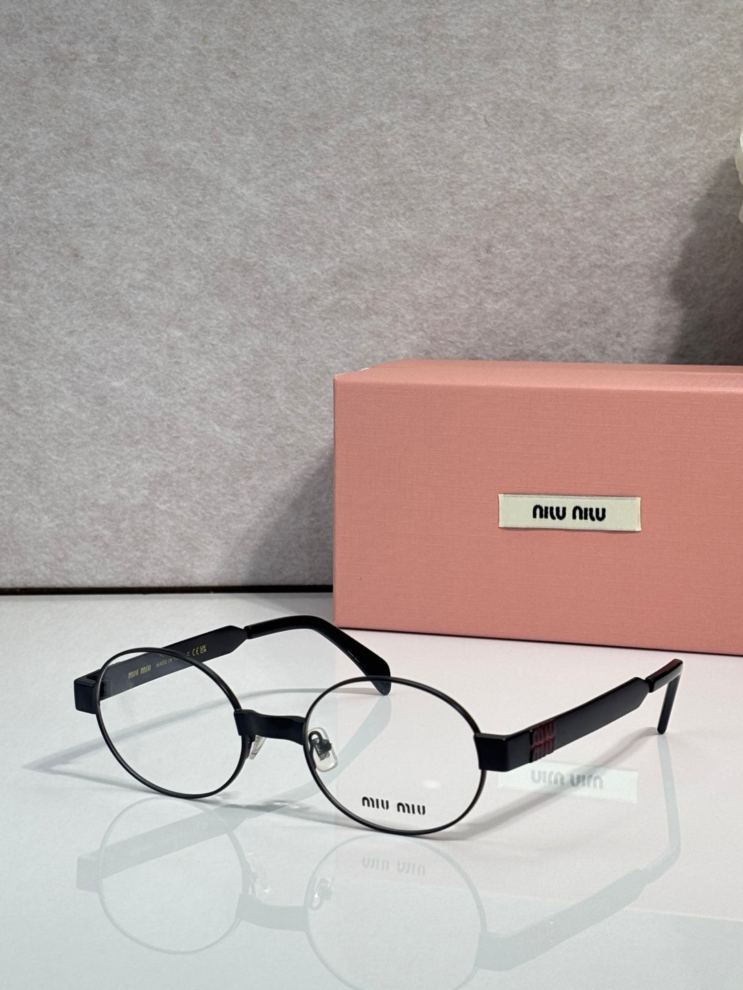 Round eyeglass frames with clear lenses, black arms and metal hinges, Miu Miu logo.