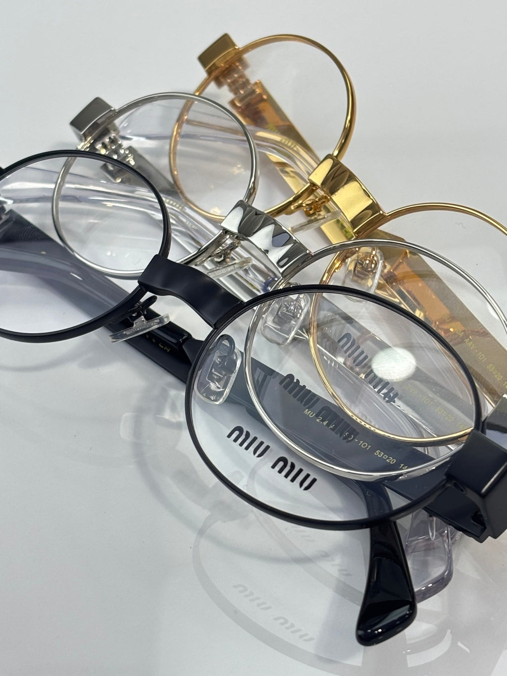 Close view of eyeglass frames with clear lenses, gold and black temples, Miu Miu logos.