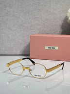 Round eyeglass frames with clear lenses, gold-toned arms, Miu Miu logo.